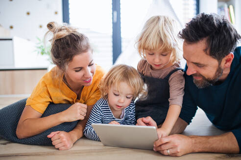 Vorderansicht einer jungen Familie mit zwei kleinen Kindern im Schlafzimmer, die ein Tablet benutzen. - HPIF17769
