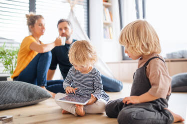 Vorderansicht einer jungen Familie mit zwei kleinen Kindern im Schlafzimmer, die ein Tablet benutzen. - HPIF17770