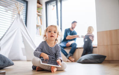 Front view of small toddler girl sitting indoors in bedroom, using tablet. - HPIF17772