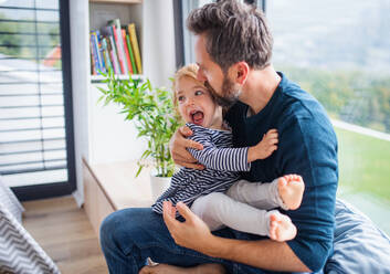 Fröhlicher junger Vater mit kleiner Tochter drinnen im Schlafzimmer beim Spielen und Umarmen. - HPIF17773