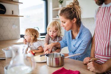 A young family with two small children indoors in kitchen, preparing food. - HPIF17777