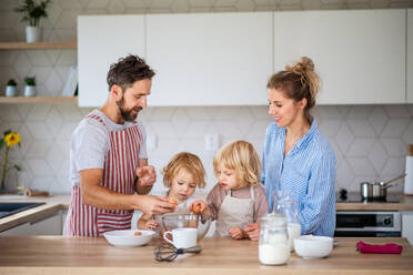 Vorderansicht einer jungen Familie mit zwei kleinen Kindern in der Küche, die beim Kochen Eier aufschlagen. - HPIF17778