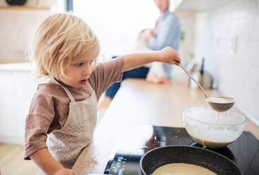 A concentrated small boy helping indoors in kitchen with making pancakes. - HPIF17792