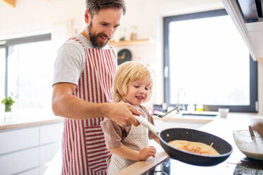 Eine Seitenansicht eines kleinen Jungen, der seinem Vater in der Küche bei der Zubereitung von Pfannkuchen hilft. - HPIF17795
