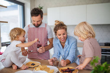 Vorderansicht einer jungen Familie mit zwei kleinen Kindern in der Küche, die Pfannkuchen essen. - HPIF17796