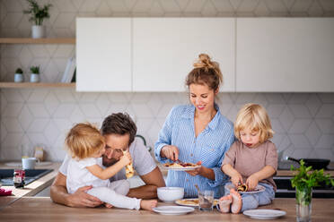 Vorderansicht einer jungen Familie mit zwei kleinen Kindern in der Küche, die Pfannkuchen essen. - HPIF17798