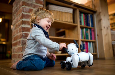 Ein glückliches süßes Kleinkind Junge stehen drinnen zu Hause, spielen mit Roboter-Hund. - HPIF17805