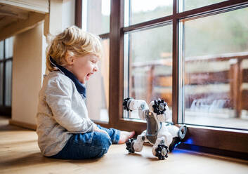 Ein glückliches süßes Kleinkind Junge sitzt auf dem Boden zu Hause, spielen mit Roboter-Hund. - HPIF17820