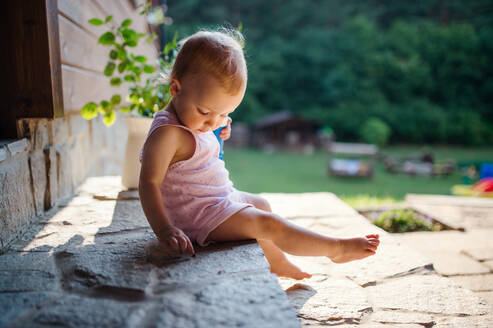 Ein süßes Kleinkind Mädchen sitzen im Freien vor dem Haus im Sommer. kopieren Raum. - HPIF17853
