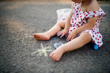 Midsection of unrecognizable toddler girl outdoors in countryside, chalk drawing on road. - HPIF17856