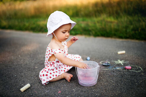 Ein süßes Kleinkind Mädchen im Freien in der Landschaft, Kreidezeichnung auf der Straße. - HPIF17858