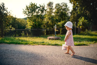 Ein süßes Kleinkind Mädchen zu Fuß im Freien auf der Straße in der Landschaft im Sommer. kopieren Raum. - HPIF17859