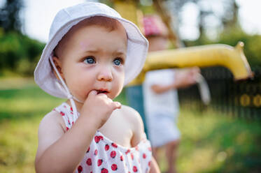 A close-up of toddler girl standing outdoors in garden in summer. Copy space. - HPIF17864