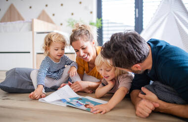 Front view of young family with two small children indoors in bedroom reading a book. - HPIF17867
