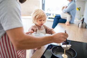 A side view of small boy helping father indoors in kitchen with making pancakes. - HPIF17873