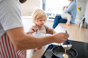 Eine Seitenansicht eines kleinen Jungen, der seinem Vater in der Küche bei der Zubereitung von Pfannkuchen hilft. - HPIF17873