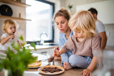 Eine junge Familie mit zwei kleinen Kindern sitzt in der Küche und isst Pfannkuchen. - HPIF17874