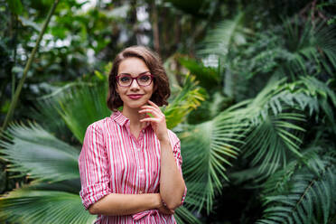 Junge Frau mit verschränkten Armen steht im botanischen Garten und schaut in die Kamera. - HPIF17905