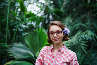 Schöne junge Frau steht im botanischen Garten und schaut in die Kamera. - HPIF17911