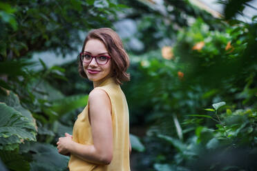 A young woman standing in botanical garden, looking at camera. Copy space. - HPIF17920