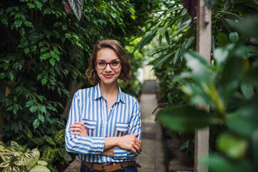 Young woman with arm crossed standing in botanical garden, looking at camera. - HPIF17931