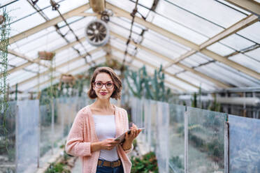 A young woman researcher standing in greenhouse, using tablet. - HPIF17937