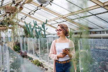 Young woman researcher standing in greenhouse in botanical garden, using tablet. - HPIF17943