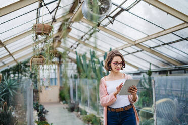 Young woman researcher standing in greenhouse in botanical garden, using tablet. - HPIF17944