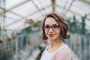 Young woman researcher standing in greenhouse in botanical garden, looking at camera. - HPIF17946