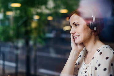 A portrait of woman with headphones sitting at the table in a cafe. Shot through glass. - HPIF17973