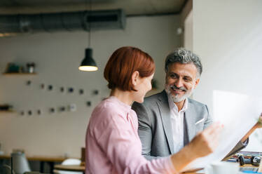 A man and woman having business meeting in a cafe, looking at blueprints. - HPIF17984