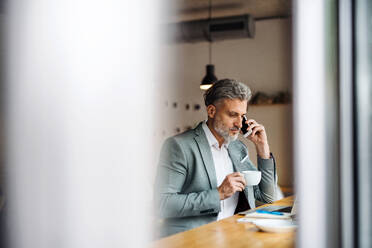 Ein reifer Mann mit Kaffee und Smartphone am Tisch in einem Café. - HPIF17987