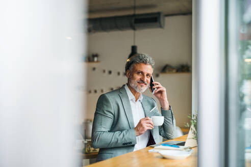 Ein reifer Mann mit Kaffee und Smartphone am Tisch in einem Café. - HPIF17988