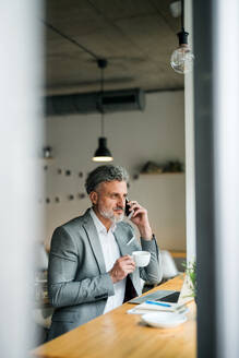 Ein reifer Mann mit Kaffee und Smartphone am Tisch in einem Café, der ein Telefongespräch führt. - HPIF17989