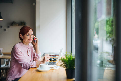 Eine attraktive Frau mit Kaffee und Telefon sitzt am Tisch eines Cafés und telefoniert. - HPIF17999