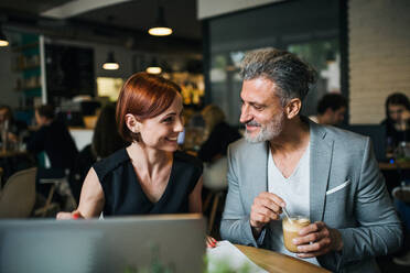 Ein Mann und eine Frau mit Kaffee bei einem Geschäftstreffen in einem Café, mit Laptop. - HPIF18007