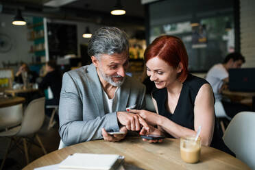 Ein Mann und eine Frau mit Kaffee bei einem Geschäftstreffen in einem Café, mit Smartphone. - HPIF18013