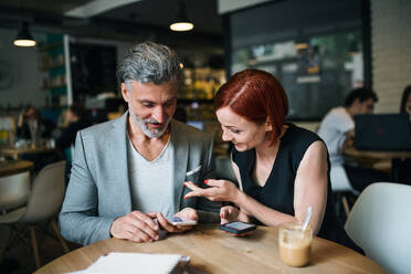 Ein Mann und eine Frau mit Kaffee bei einem Geschäftstreffen in einem Café, mit Smartphone. - HPIF18014