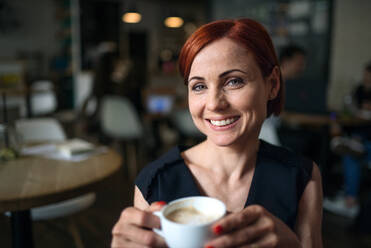 Porträt einer attraktiven Frau, die in einem Café sitzt und eine Tasse Kaffee in der Hand hält. - HPIF18027