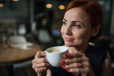 Porträt einer attraktiven Frau, die in einem Café sitzt und eine Tasse Kaffee in der Hand hält. - HPIF18028