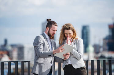 Zwei fröhliche junge Geschäftsleute mit Tablet stehen auf einer Terrasse vor einem Büro und arbeiten. - HPIF18031