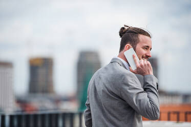 Ein junger Geschäftsmann mit Smartphone steht auf einer Terrasse vor seinem Büro und führt ein Telefongespräch. - HPIF18036