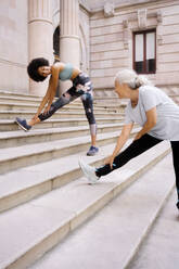 Lächelnde Frau beim Sport mit ihrer Mutter auf einer Treppe in der Nähe eines Gebäudes - MMPF00758