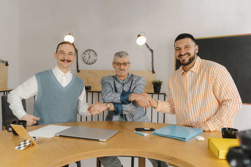 Drei männliche Kollegen unterschiedlichen Alters und unterschiedlicher Nationalität schütteln sich im Studio die Hände - EHAF00022