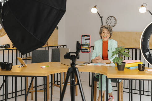 Geschäftsfrau, die einen Online-Kurs aufnimmt, sitzt am Tisch im Studio - EHAF00034