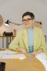 Geschäftsfrau mit Brille sitzt am Tisch im Studio - EHAF00038