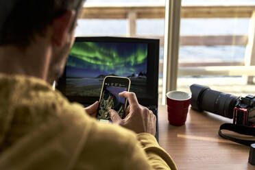 One man looking at maps on smart phone while working with laptop computer, Lofoten Islands, Norway, Scandinavia, Europe - RHPLF24110