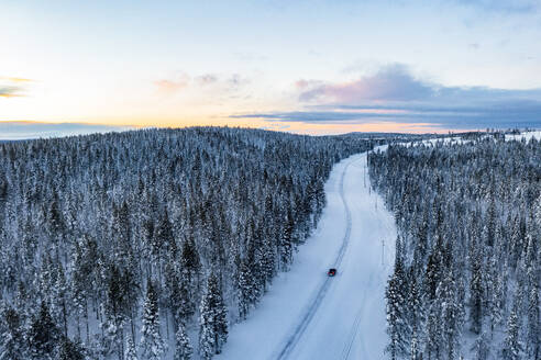 Auto fährt in den verschneiten Wald bei Sonnenuntergang, Luftaufnahme, Gallivare, Landkreis Norrbotten, Lappland, Schweden, Skandinavien, Europa - RHPLF24112