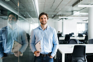 A portrait of young businessman standing in an office, looking at camera. - HPIF18049