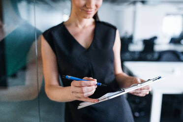Ein Mittelteil einer jungen Geschäftsfrau mit Klemmbrett in einem Büro, stehend. - HPIF18051